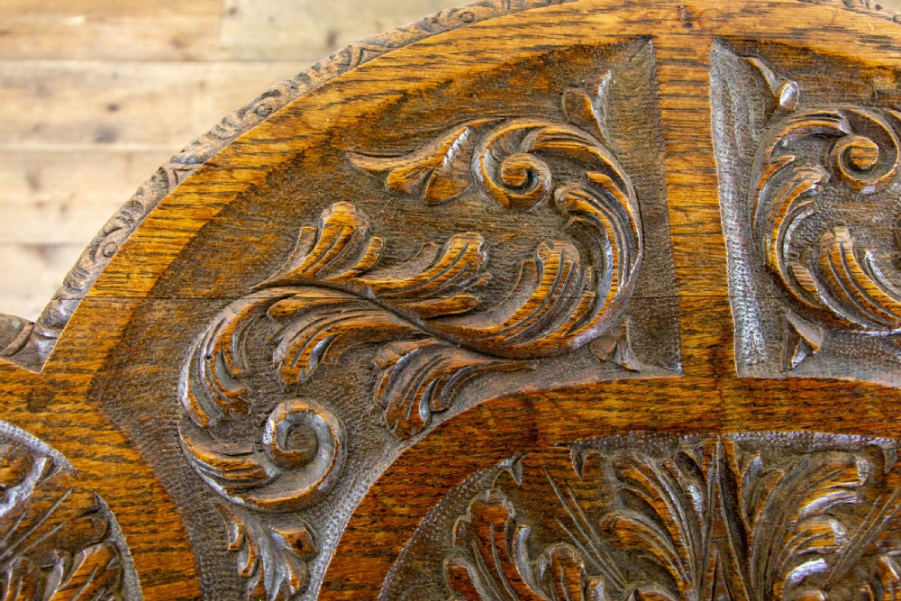 A carved oak side table featuring a lobed, relief-carved top with floral motifs, four turned legs, and a carved lower tier shelf. View X