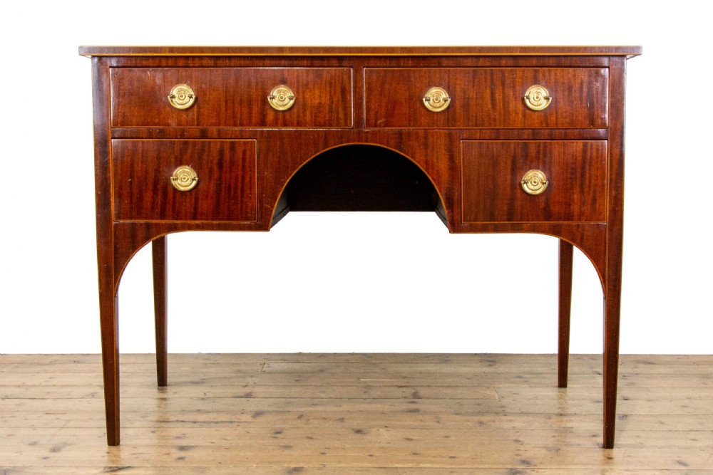 An antique Sheraton Revival mahogany side table featuring four drawers, string inlay detailing, brass ring handles, and an arched central kneehole on tapered square legs.