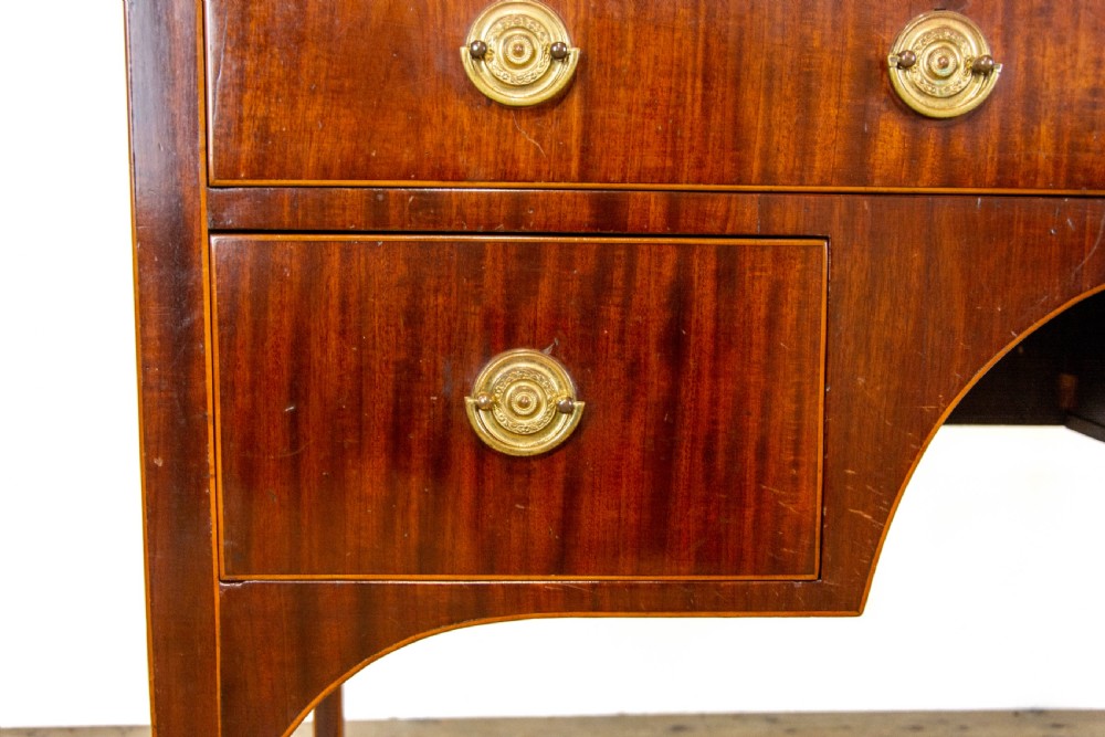 An antique Sheraton Revival mahogany side table featuring four drawers, string inlay detailing, brass ring handles, and an arched central kneehole on tapered square legs. View IV