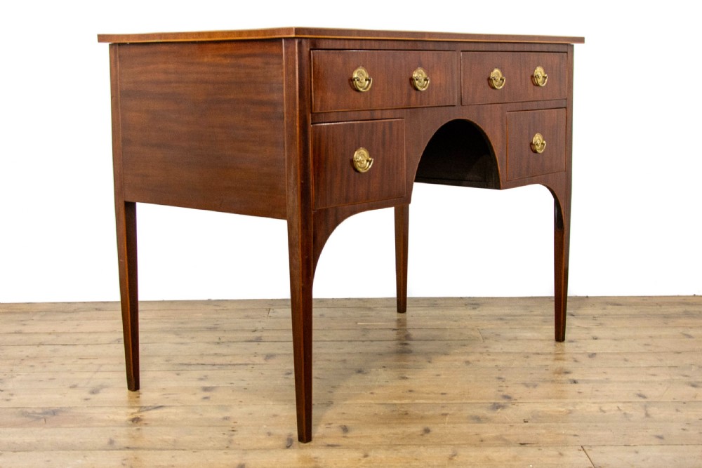An antique Sheraton Revival mahogany side table featuring four drawers, string inlay detailing, brass ring handles, and an arched central kneehole on tapered square legs. View VI