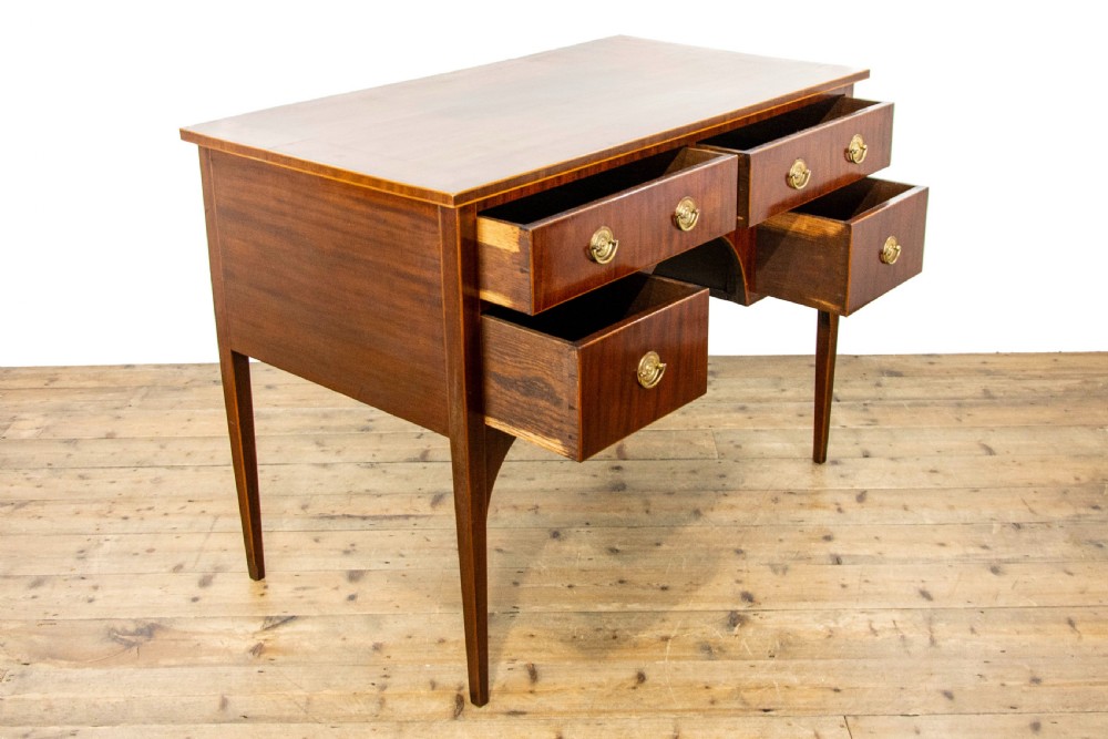 An antique Sheraton Revival mahogany side table featuring four drawers, string inlay detailing, brass ring handles, and an arched central kneehole on tapered square legs. View VII