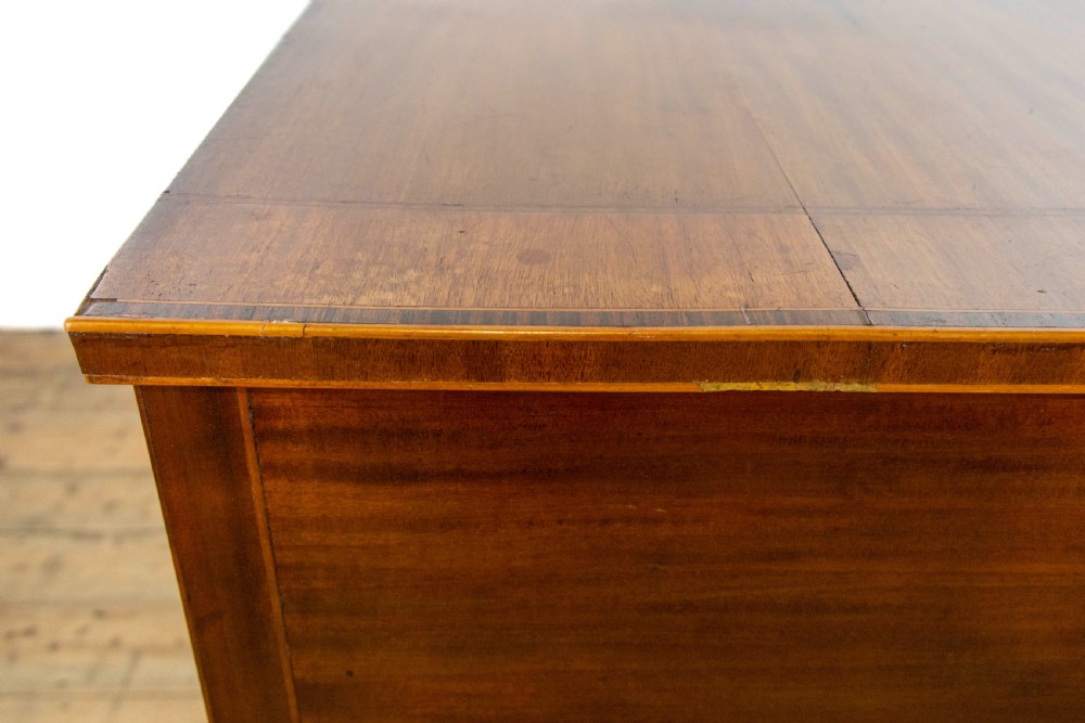 An antique Sheraton Revival mahogany side table featuring four drawers, string inlay detailing, brass ring handles, and an arched central kneehole on tapered square legs. View IX
