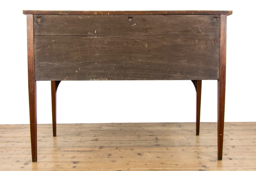 An antique Sheraton Revival mahogany side table featuring four drawers, string inlay detailing, brass ring handles, and an arched central kneehole on tapered square legs. View X