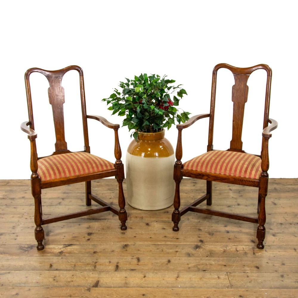 A pair of antique oak armchairs featuring shaped splat backs, curved armrests, turned legs, and red striped upholstered seats.