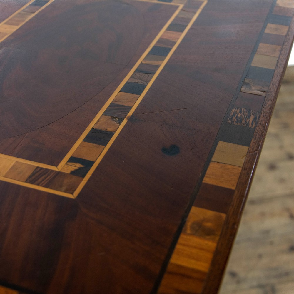 A dark brown mahogany side table featuring a rectangular top with geometric timber inlay, a central octagonal column, and a four-pointed pedestal base. View VI