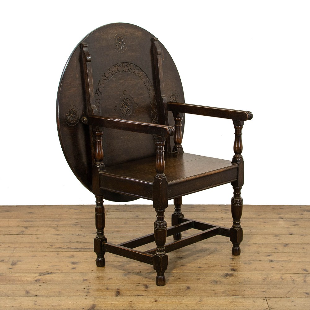 A dark oak monks bench featuring a circular carved tilt-top backrest, turned arm supports, and a solid seat raised on turned legs.