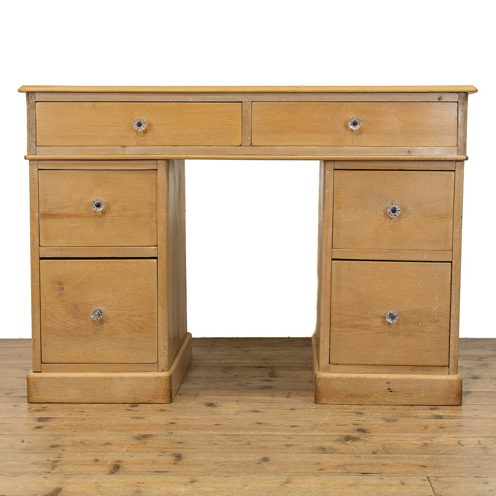 An antique natural pine kneehole desk featuring twin pedestals, six lower drawers, two upper frieze drawers, and clear glass knobs.
