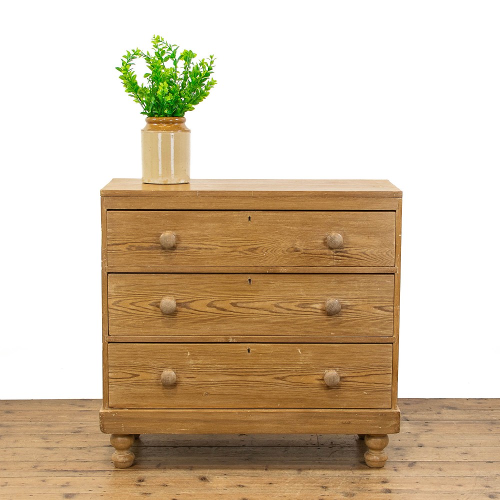A Victorian waxed pine chest of drawers with three full-width drawers, turned wooden handles, and bun feet.