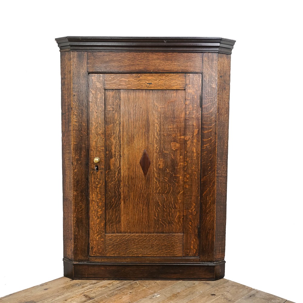An antique Georgian dark oak wall-hanging corner cupboard featuring a moulded top cornice, a single fielded panel door with a central inlaid diamond motif, and a brass keyhole.