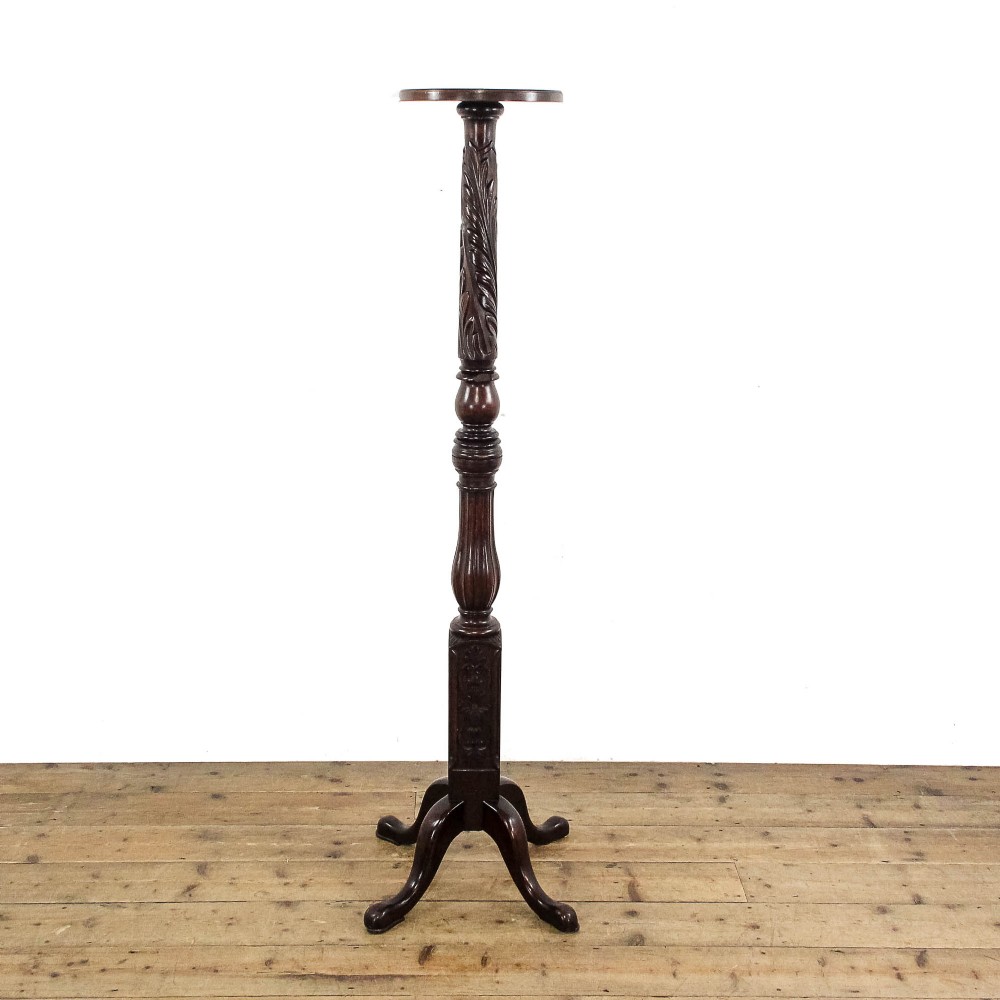 A tall dark mahogany torchere stand featuring a circular top, carved acanthus leaf shaft, fluted stem, and a tripod base.