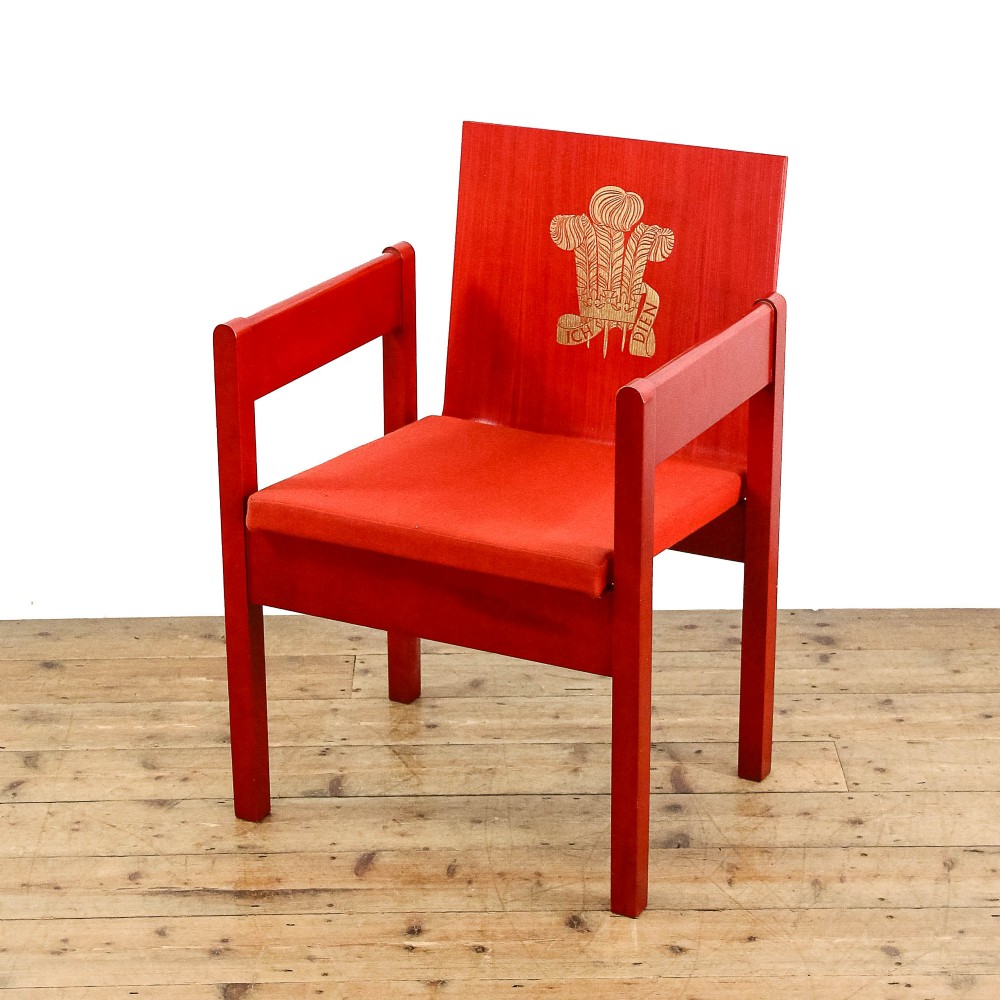 A mid-century modern vermilion red wooden armchair featuring a flat square backrest printed with a gold Prince of Wales crest.