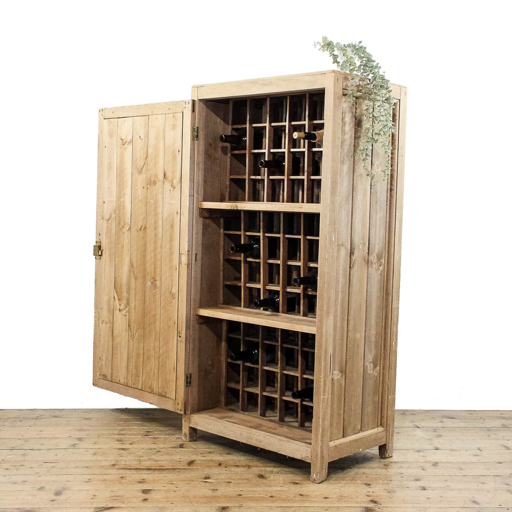 A rustic standing pine cupboard with an open single plank door revealing three sections of fitted wooden lattice bottle racks.