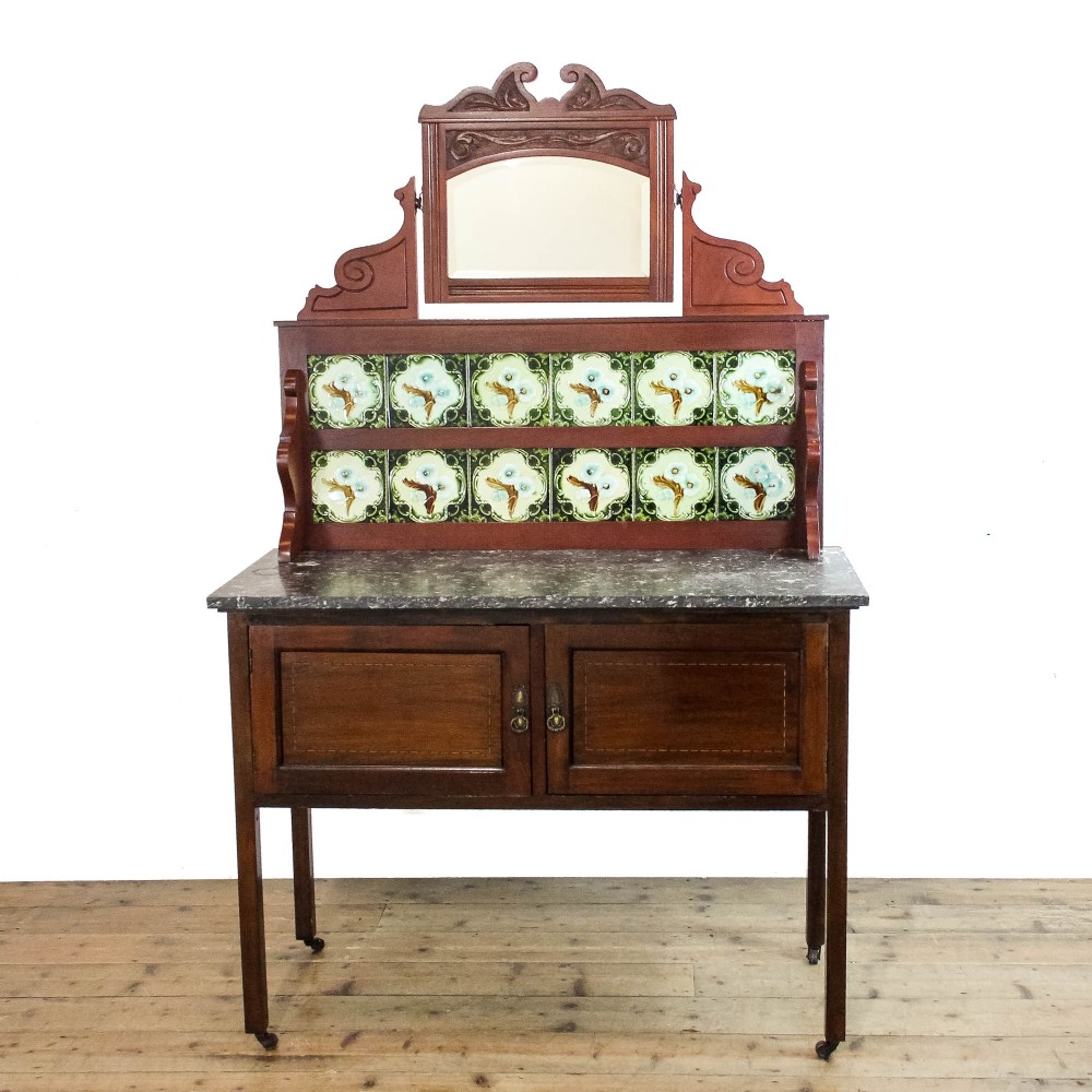 An Edwardian mahogany washstand with a grey marble top, a green ceramic tiled splashback, and an arch-framed mirror above a two-door cabinet on castors.
