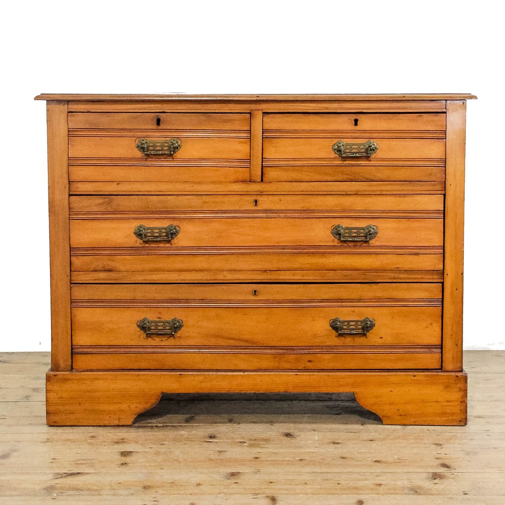 An Edwardian satinwood chest of drawers featuring two short over two long reeded drawers with ornate brass handles.