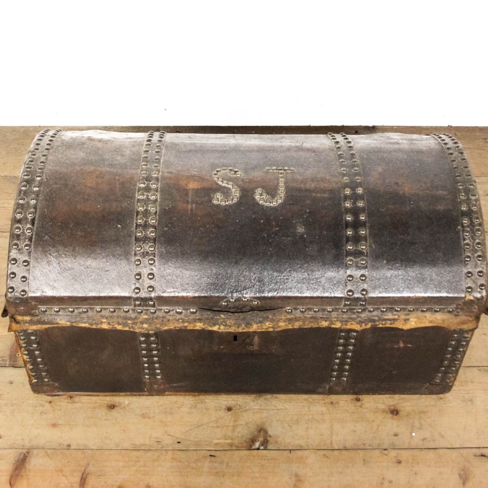 An antique dark brown leather domed trunk decorated with metal studs and initials on the curved lid.