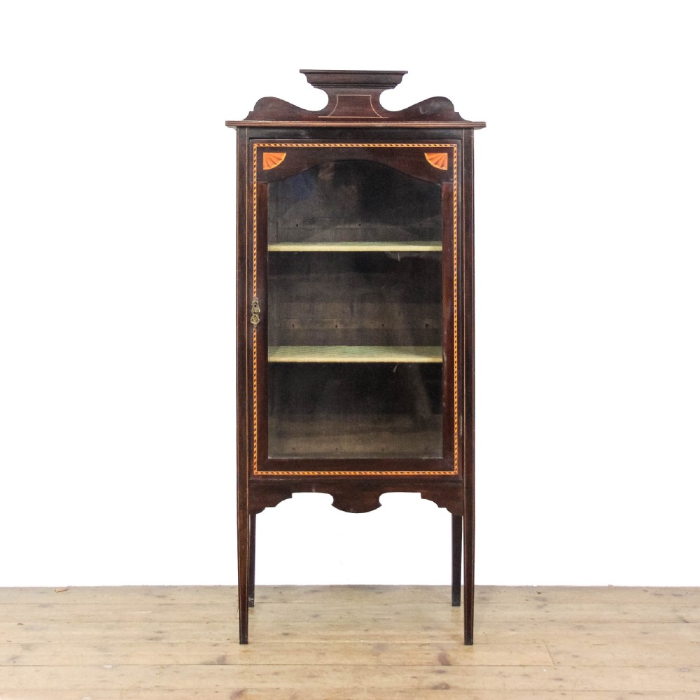 An Edwardian dark mahogany single door display cabinet featuring delicate satinwood inlay, fan corner marquetry, a shaped pediment, and square tapered legs.