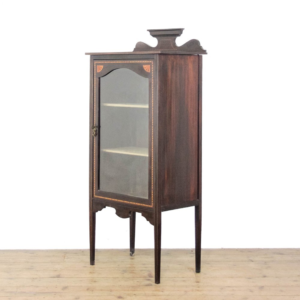 An Edwardian dark mahogany single door display cabinet featuring delicate satinwood inlay, fan corner marquetry, a shaped pediment, and square tapered legs. View V