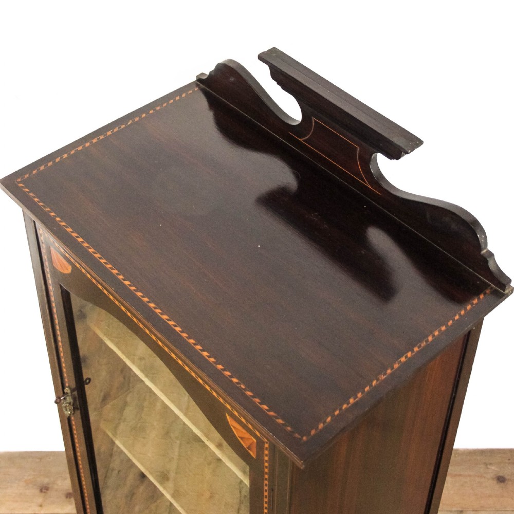 An Edwardian dark mahogany single door display cabinet featuring delicate satinwood inlay, fan corner marquetry, a shaped pediment, and square tapered legs. View VI