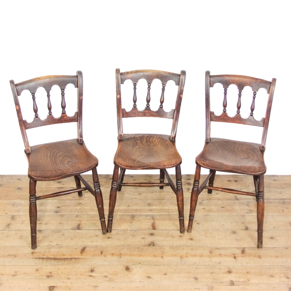 A set of three Victorian elm farmhouse dining chairs featuring shaped seats, turned spindles, and dark timber finishes.