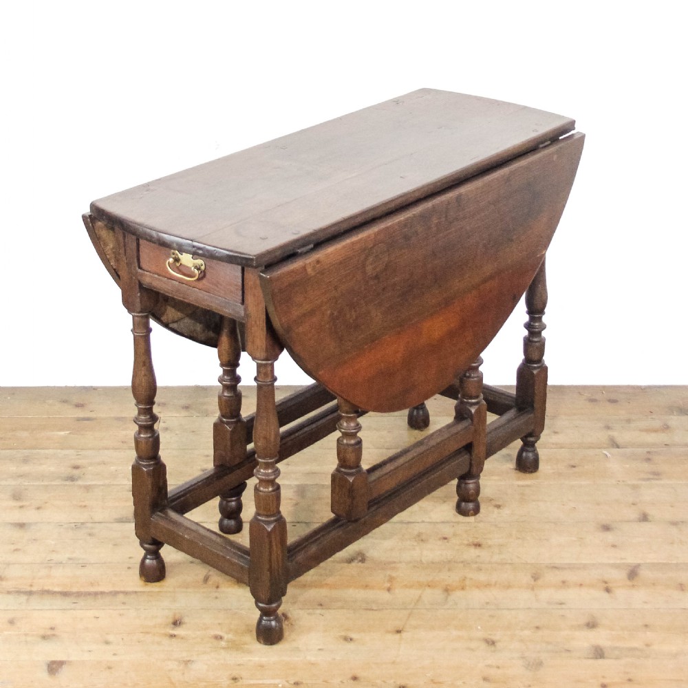 An antique dark oak gateleg table featuring two hinged drop leaves, turned legs, lower stretchers, and a single end drawer with a brass handle. View II