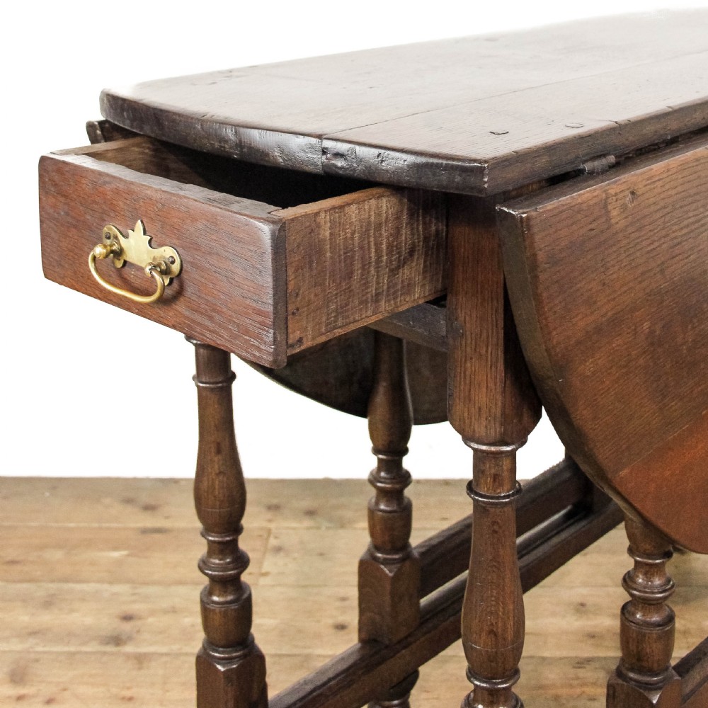 An antique dark oak gateleg table featuring two hinged drop leaves, turned legs, lower stretchers, and a single end drawer with a brass handle. View III