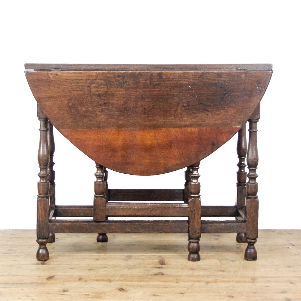 An antique dark oak gateleg table featuring two hinged drop leaves, turned legs, lower stretchers, and a single end drawer with a brass handle. View IV