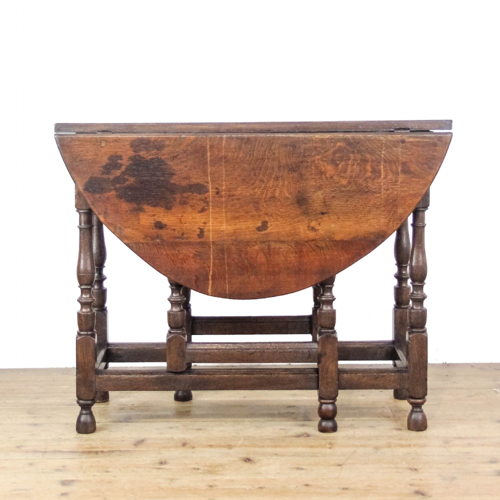 An antique dark oak gateleg table featuring two hinged drop leaves, turned legs, lower stretchers, and a single end drawer with a brass handle. View V