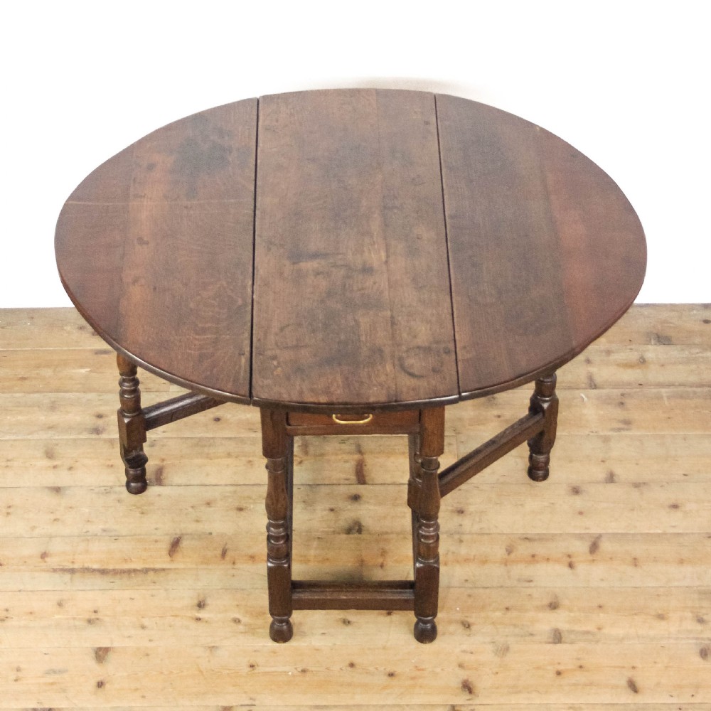 An antique dark oak gateleg table featuring two hinged drop leaves, turned legs, lower stretchers, and a single end drawer with a brass handle. View VII