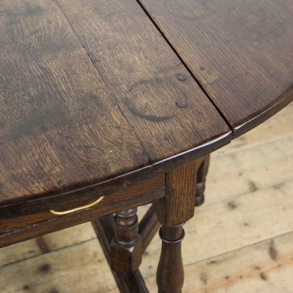 An antique dark oak gateleg table featuring two hinged drop leaves, turned legs, lower stretchers, and a single end drawer with a brass handle. View IX