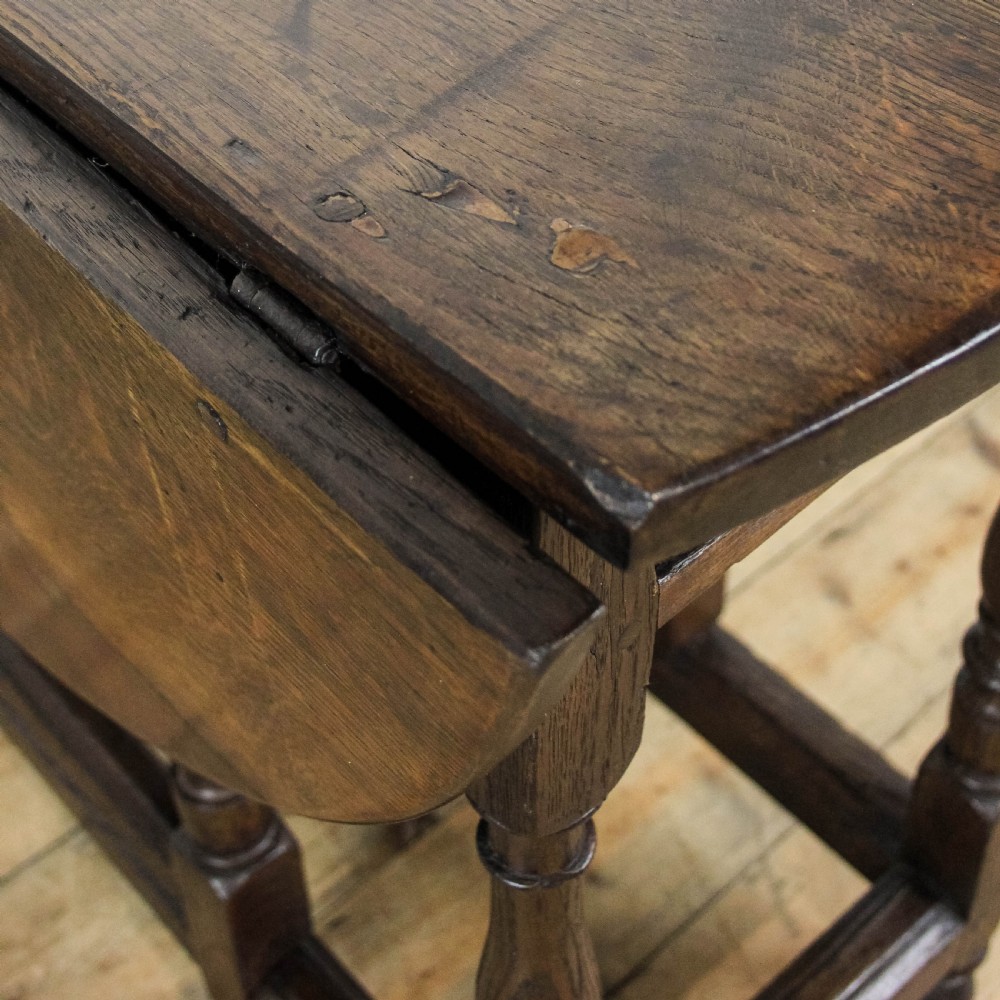 An antique dark oak gateleg table featuring two hinged drop leaves, turned legs, lower stretchers, and a single end drawer with a brass handle. View X