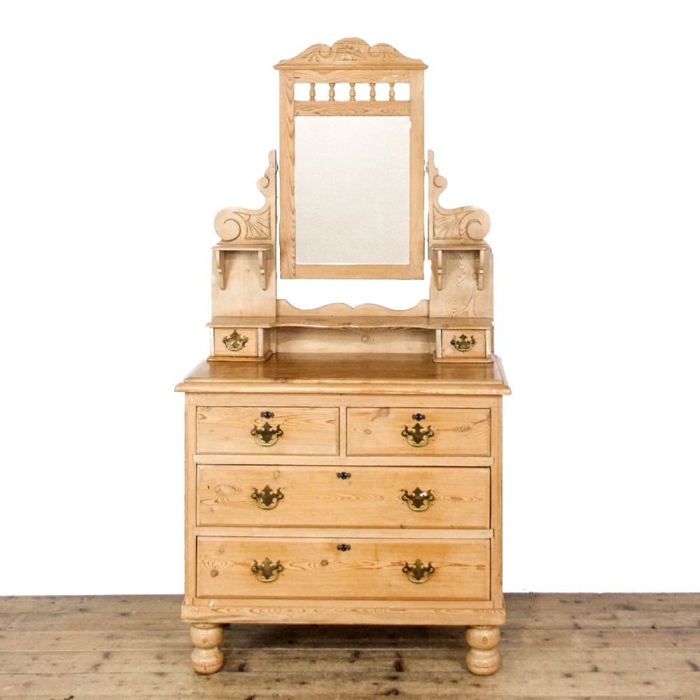 An antique pine dressing chest featuring an upper swivel mirror, small gallery drawers, two short drawers over two long drawers, and turned feet.