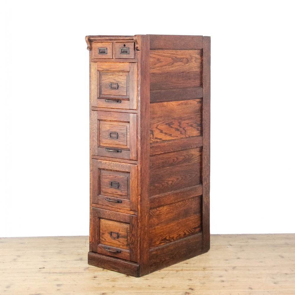 A tall early 20th-century oak filing cabinet featuring panelled sides, four large drawers, two small top drawers, and metal pull handles.
