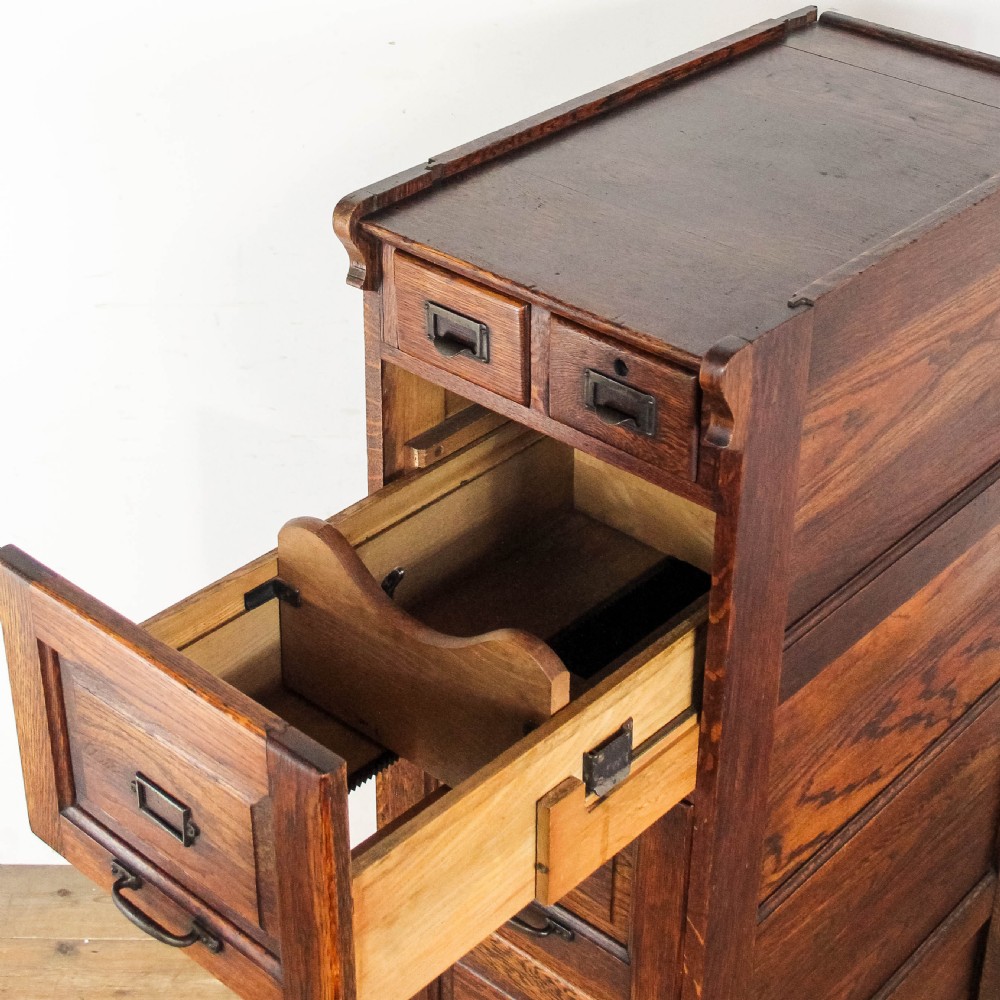 A tall early 20th-century oak filing cabinet featuring panelled sides, four large drawers, two small top drawers, and metal pull handles. View IV