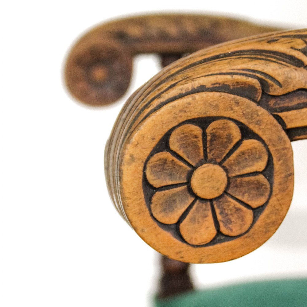 A high-backed Victorian armchair with green velvet upholstery, intricately carved wooden scroll arms, decorative front stretcher, and turned legs. View IV