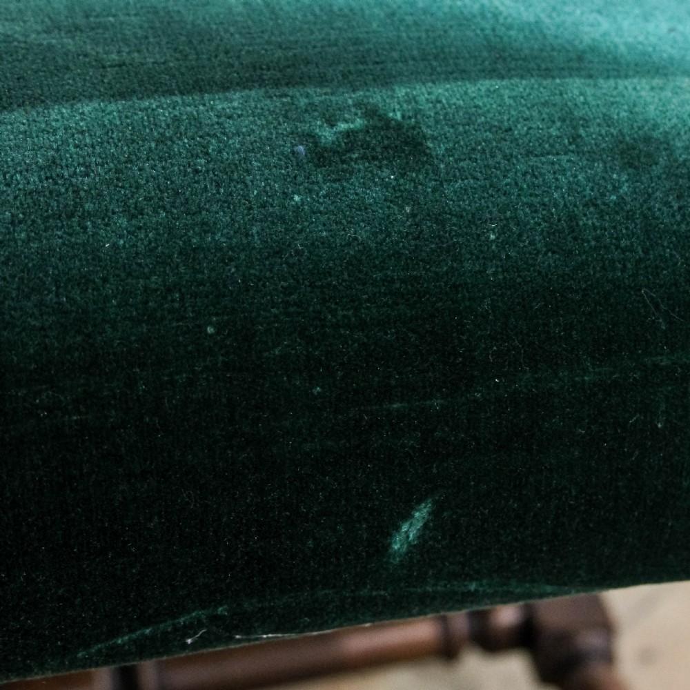 A high-backed Victorian armchair with green velvet upholstery, intricately carved wooden scroll arms, decorative front stretcher, and turned legs. View X