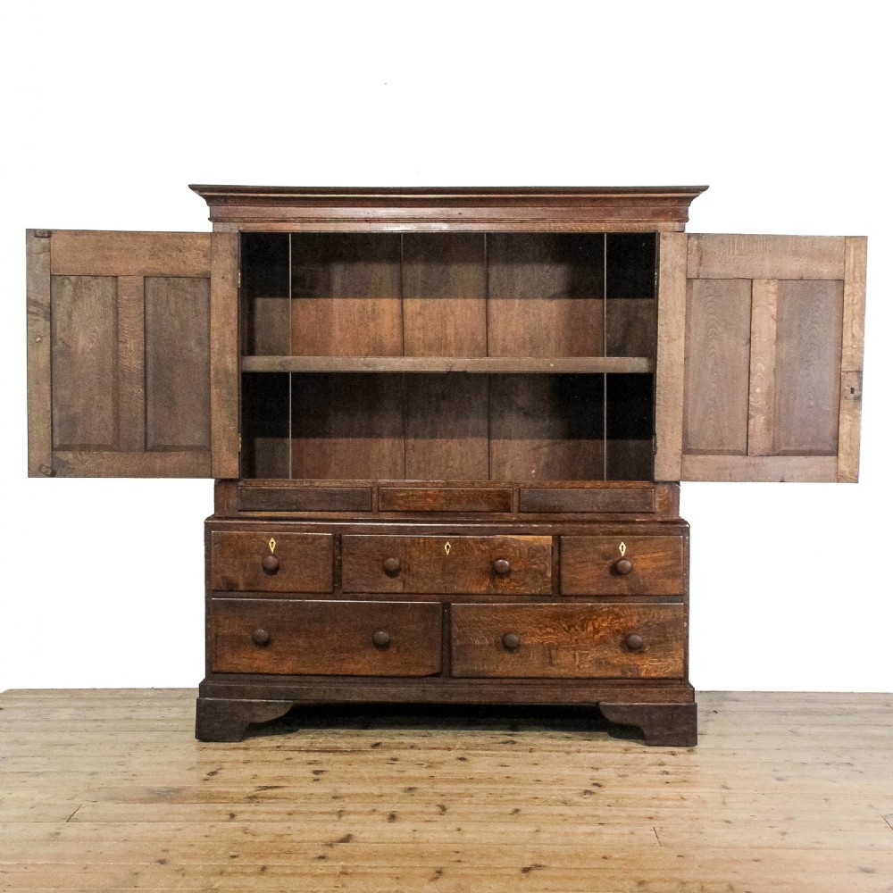 An early nineteenth-century dark oak Welsh press cupboard with two arched fielded panel doors above a base of five drawers on bracket feet. View II