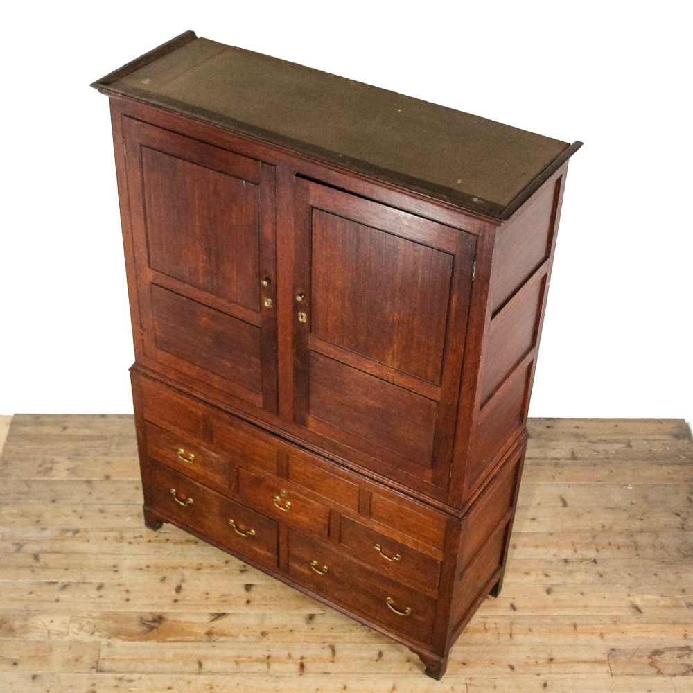 An antique dark oak linen press cabinet featuring two panelled upper doors above a lower chest containing seven drawers with brass swan-neck handles. View III