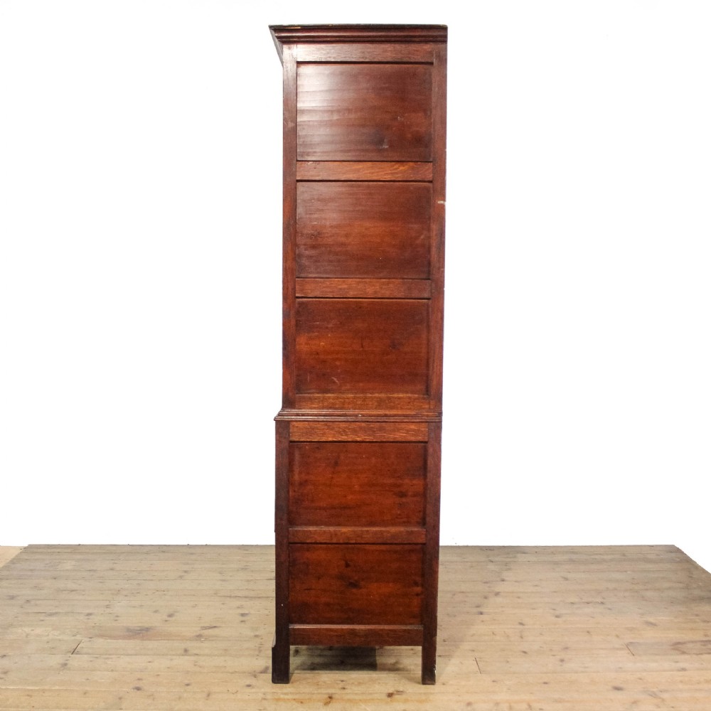 An antique dark oak linen press cabinet featuring two panelled upper doors above a lower chest containing seven drawers with brass swan-neck handles. View IV