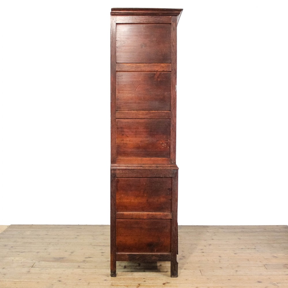 An antique dark oak linen press cabinet featuring two panelled upper doors above a lower chest containing seven drawers with brass swan-neck handles. View V
