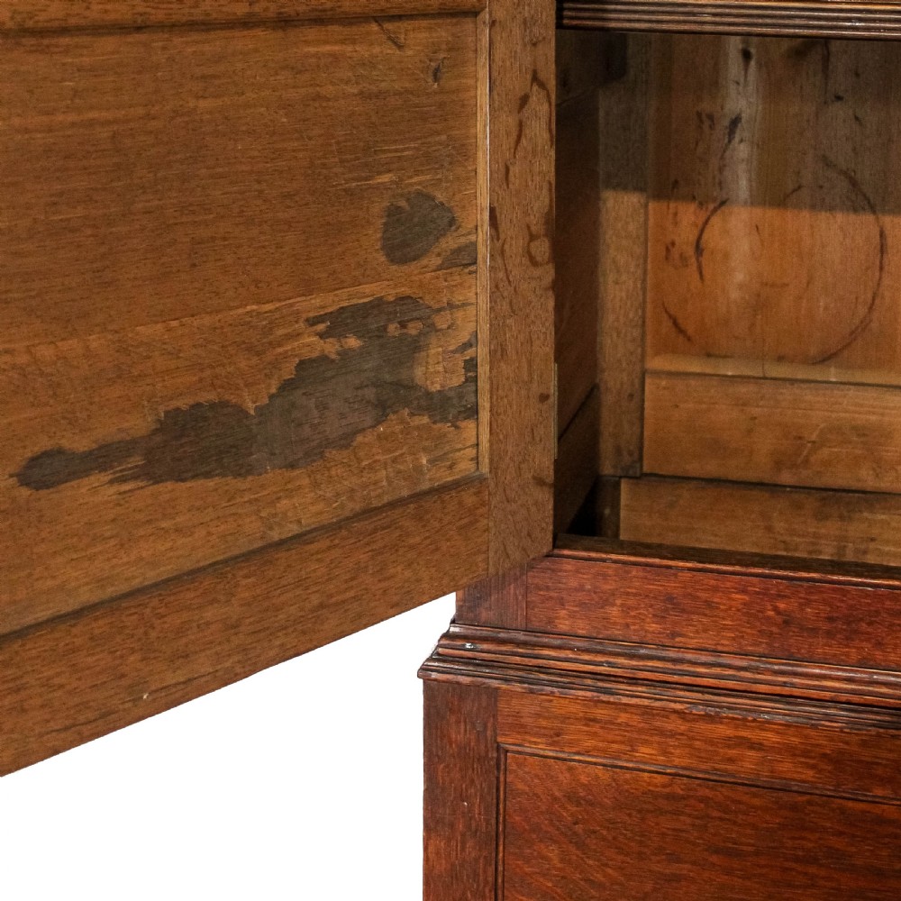 An antique dark oak linen press cabinet featuring two panelled upper doors above a lower chest containing seven drawers with brass swan-neck handles. View VIII