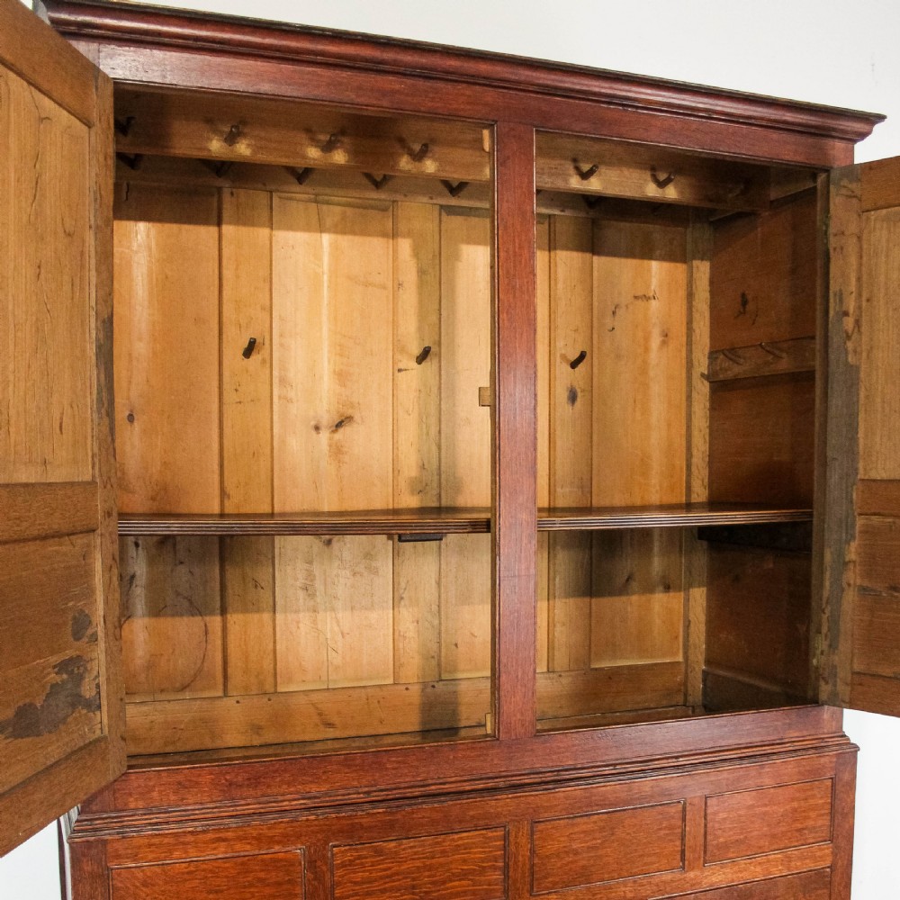 An antique dark oak linen press cabinet featuring two panelled upper doors above a lower chest containing seven drawers with brass swan-neck handles. View X