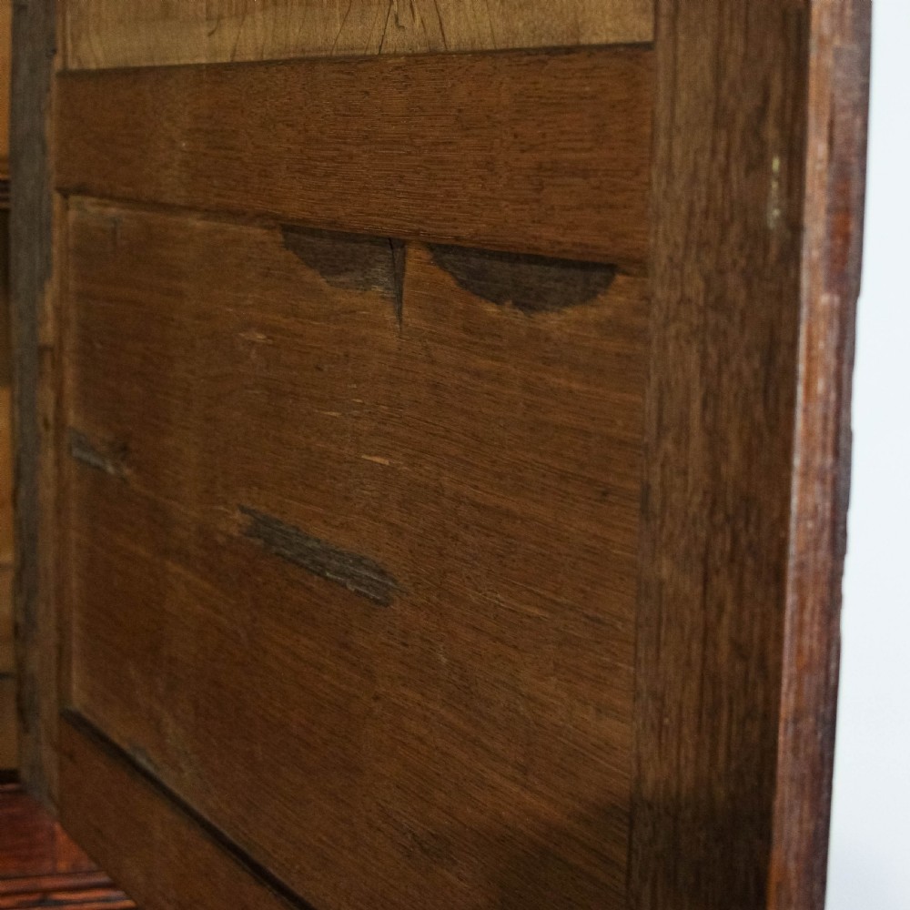 An antique dark oak linen press cabinet featuring two panelled upper doors above a lower chest containing seven drawers with brass swan-neck handles. View XIV