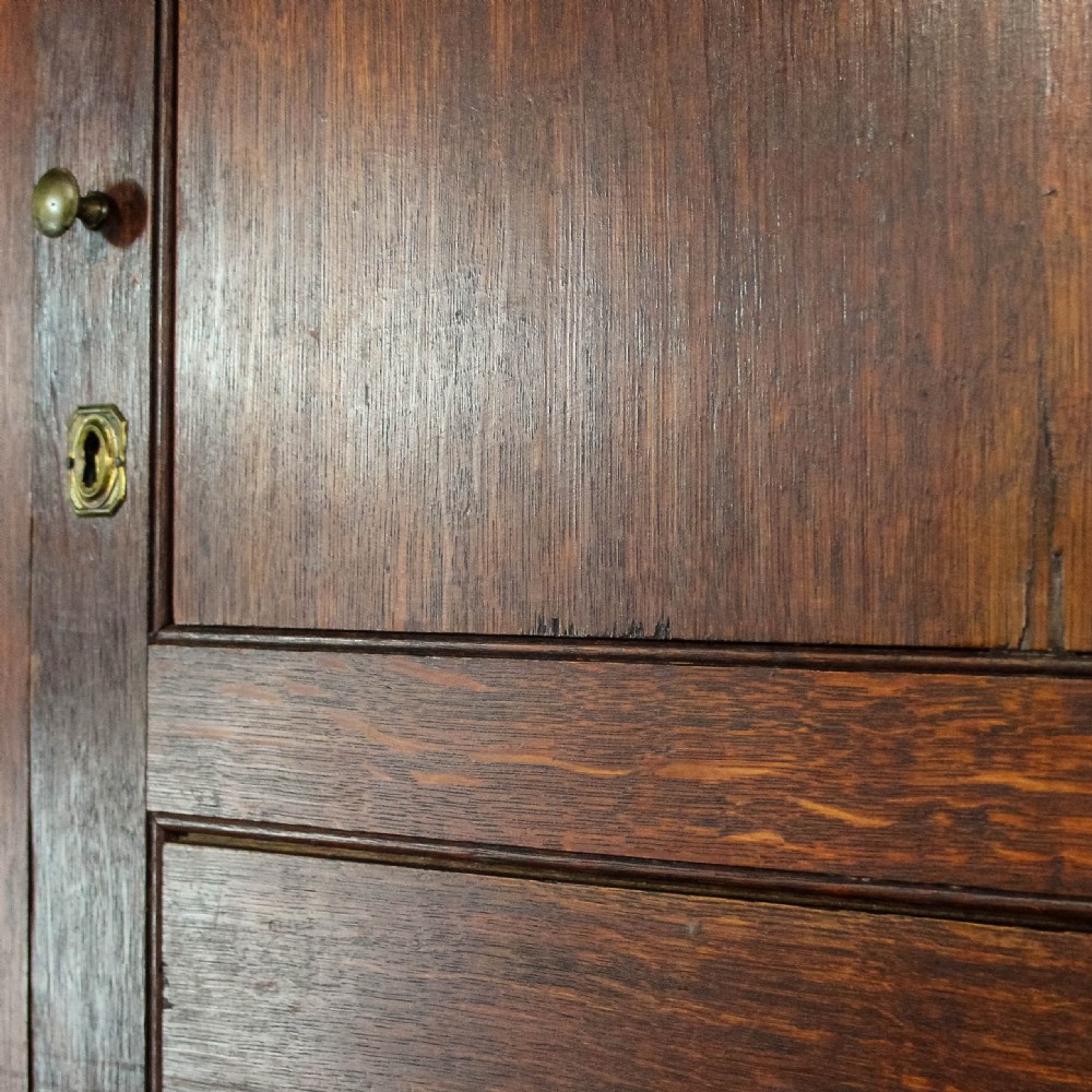 An antique dark oak linen press cabinet featuring two panelled upper doors above a lower chest containing seven drawers with brass swan-neck handles. View XV