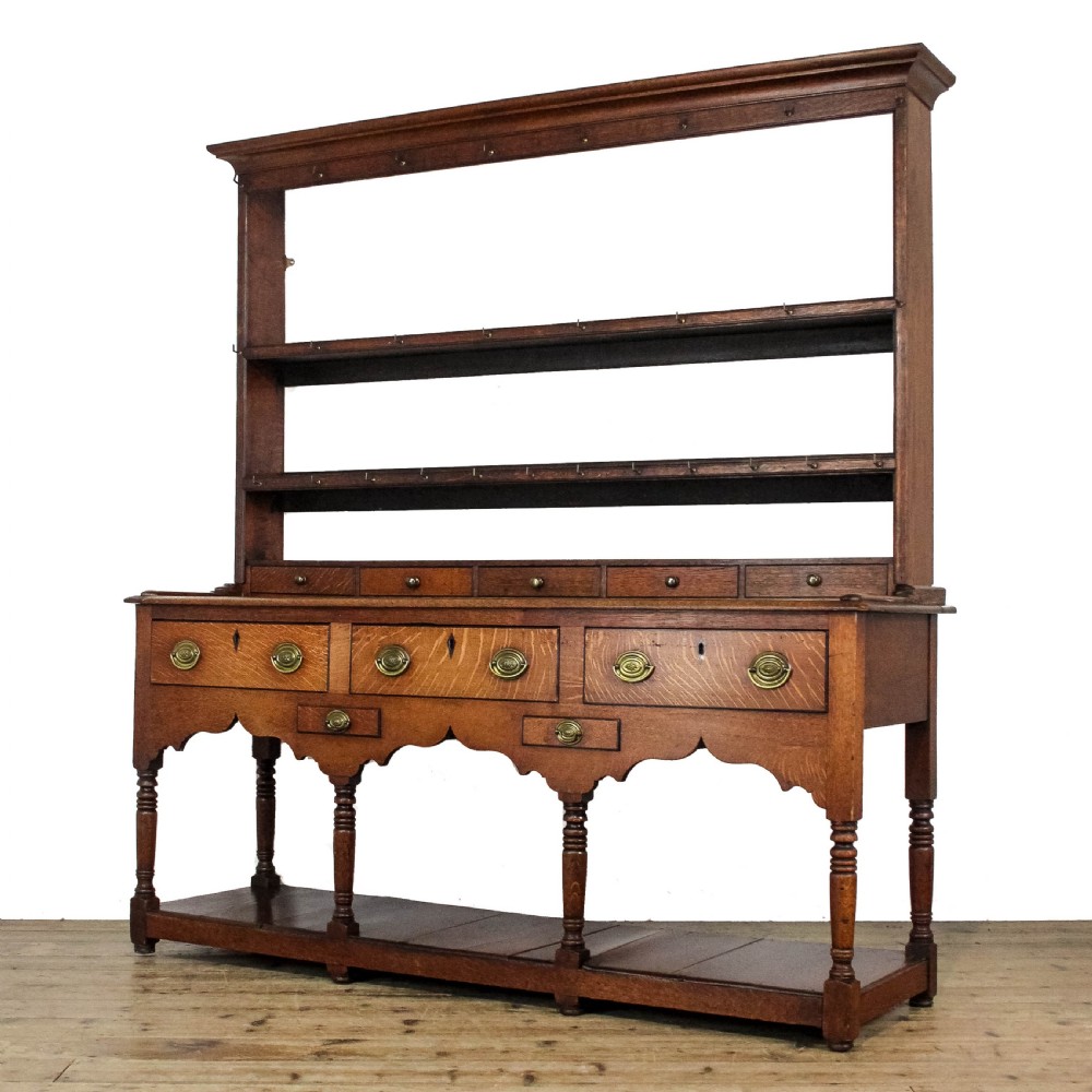 An 18th-century Welsh oak dresser featuring a three-shelf open plate rack with cup hooks, five small spice drawers, three main drawers with brass handles, a shaped apron, turned front supports, and a lower potboard shelf. View II