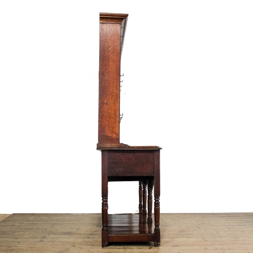 An 18th-century Welsh oak dresser featuring a three-shelf open plate rack with cup hooks, five small spice drawers, three main drawers with brass handles, a shaped apron, turned front supports, and a lower potboard shelf. View IV