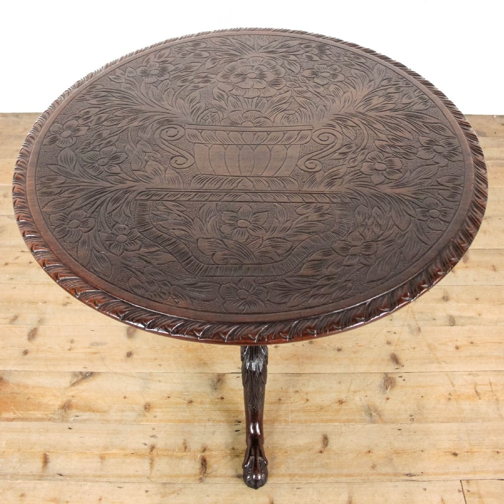 A dark mahogany tilt-top tripod table featuring an intricately carved circular top with a floral vase motif, supported on three carved legs. View II