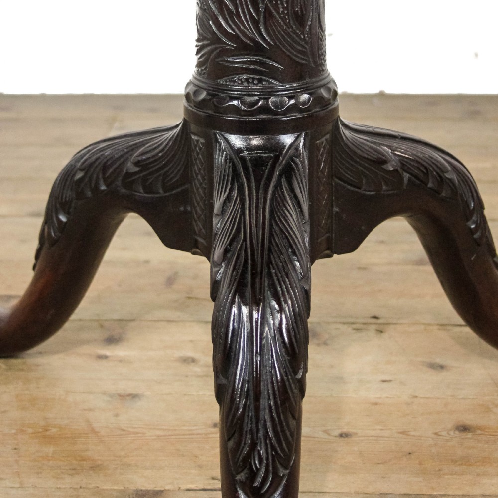 A dark mahogany tilt-top tripod table featuring an intricately carved circular top with a floral vase motif, supported on three carved legs. View IV