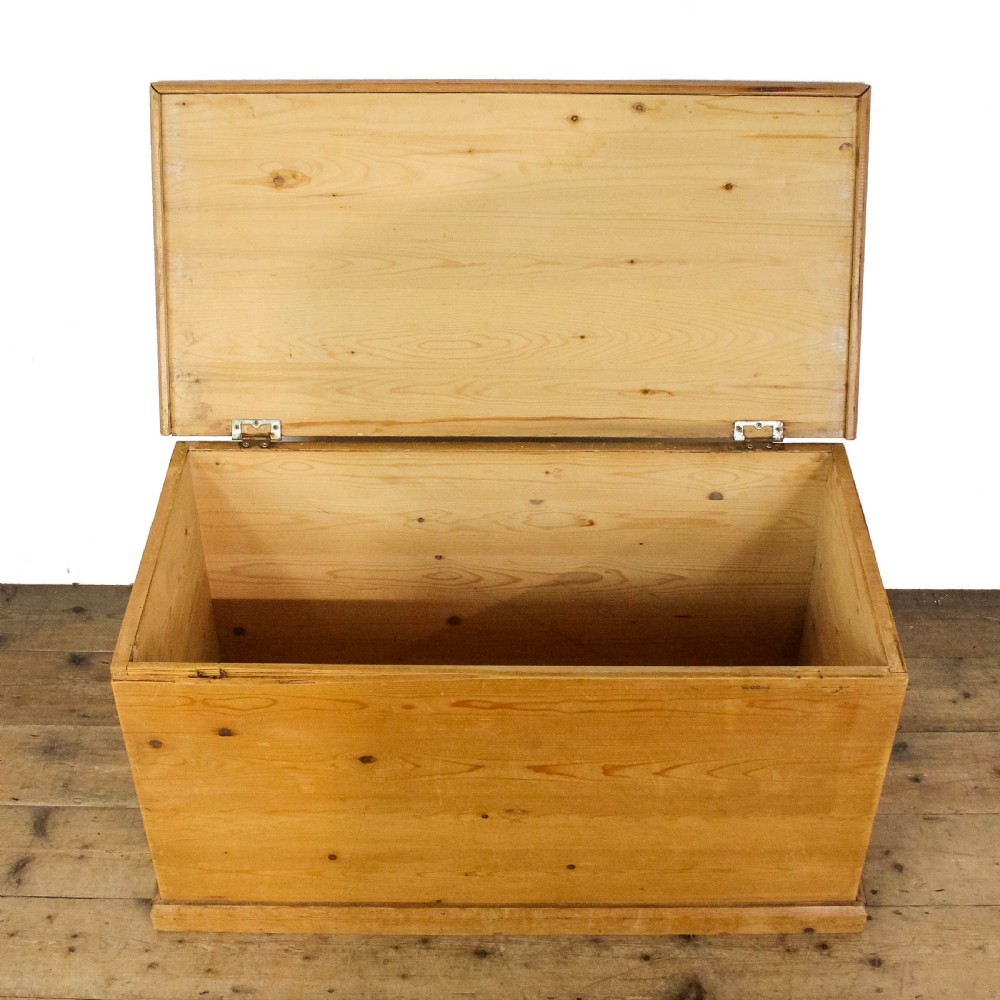 A rectangular antique pine storage trunk featuring a flat hinged lid, natural wood grain with visible knots, and a solid plinth base. View VI