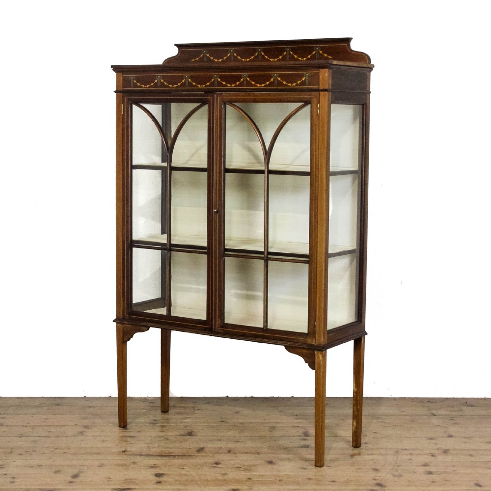 An antique Edwardian mahogany display cabinet featuring inlaid garland swags on the top frieze, twin glazed doors with gothic astragal bars, and slender square legs. View V