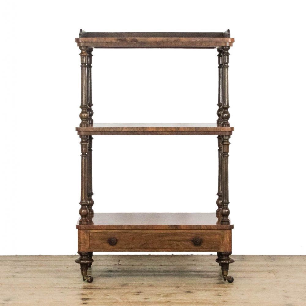 A three-tiered Victorian walnut whatnot stand featuring turned support columns, a single base drawer with turned wooden knobs, and brass castors.
